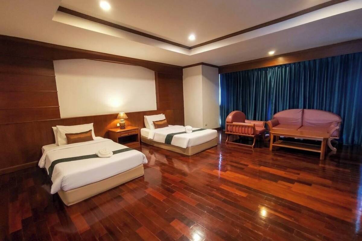 Habitación de hotel con dos camas, una zona de estar y un ventanal con cortinas.