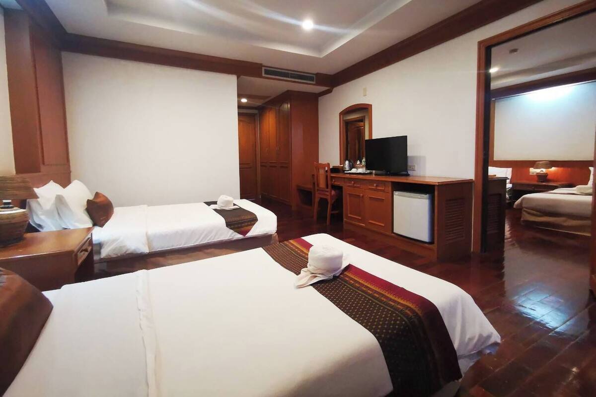 Habitación de hotel con dos camas, un escritorio con televisor, un espejo y un armario.