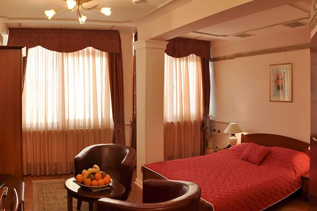 Una habitación de hotel con una cama, una silla, una mesa con fruta y una lámpara.