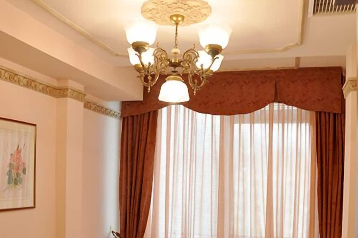 Una habitación de hotel con una cama grande, un candelabro, cortinas y un cuadro en la pared.