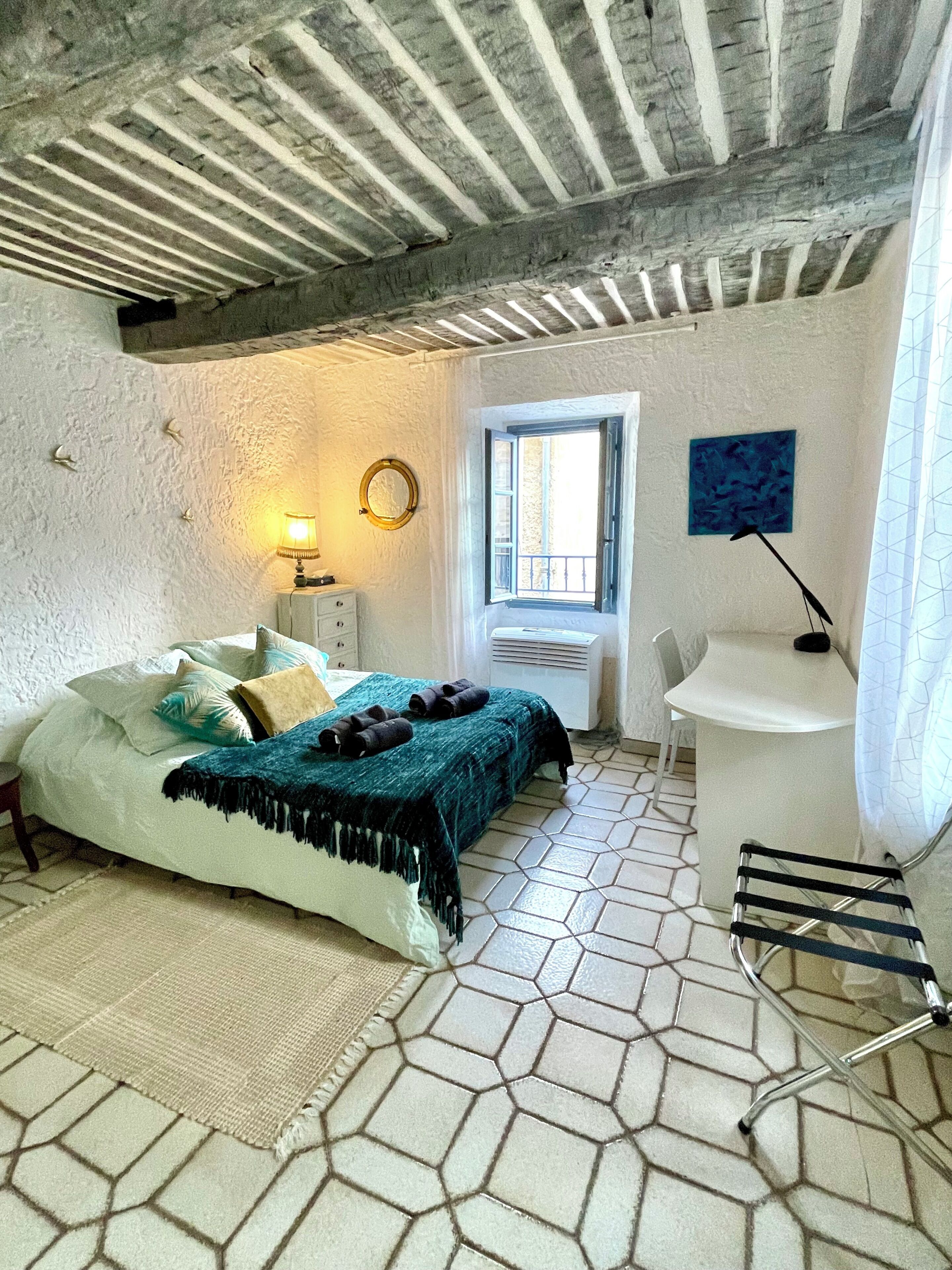 Un dormitorio con cama, mesita de noche, lámpara, ventana, silla y perchero.