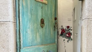 Une porte de couleur turquoise ornée d’un chat et de fleurs peintes, un sol à carreaux et un mur dont la peinture s’écaillait.