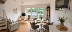 Ein modernes Wohnzimmer mit Esstisch für vier Personen, einer Couch, einem Fernseher und einer Treppe.