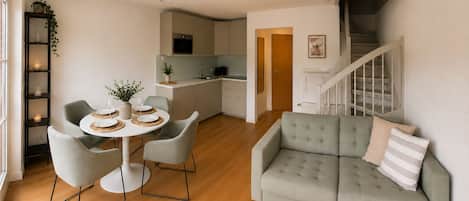 Een moderne woonkamer met een grijze bank, een eettafel gedekt voor twee personen en een keuken op de achtergrond.