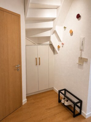 Ein Flur mit einer Holztür, weißen Schränken, einem Schuhregal und einem an der Wand befestigten Telefon.