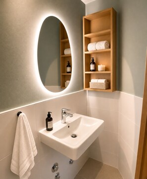 Ein Badezimmer mit einem weißen Waschbecken, einem Spiegel und einem Holzregal mit Pflegeprodukten.