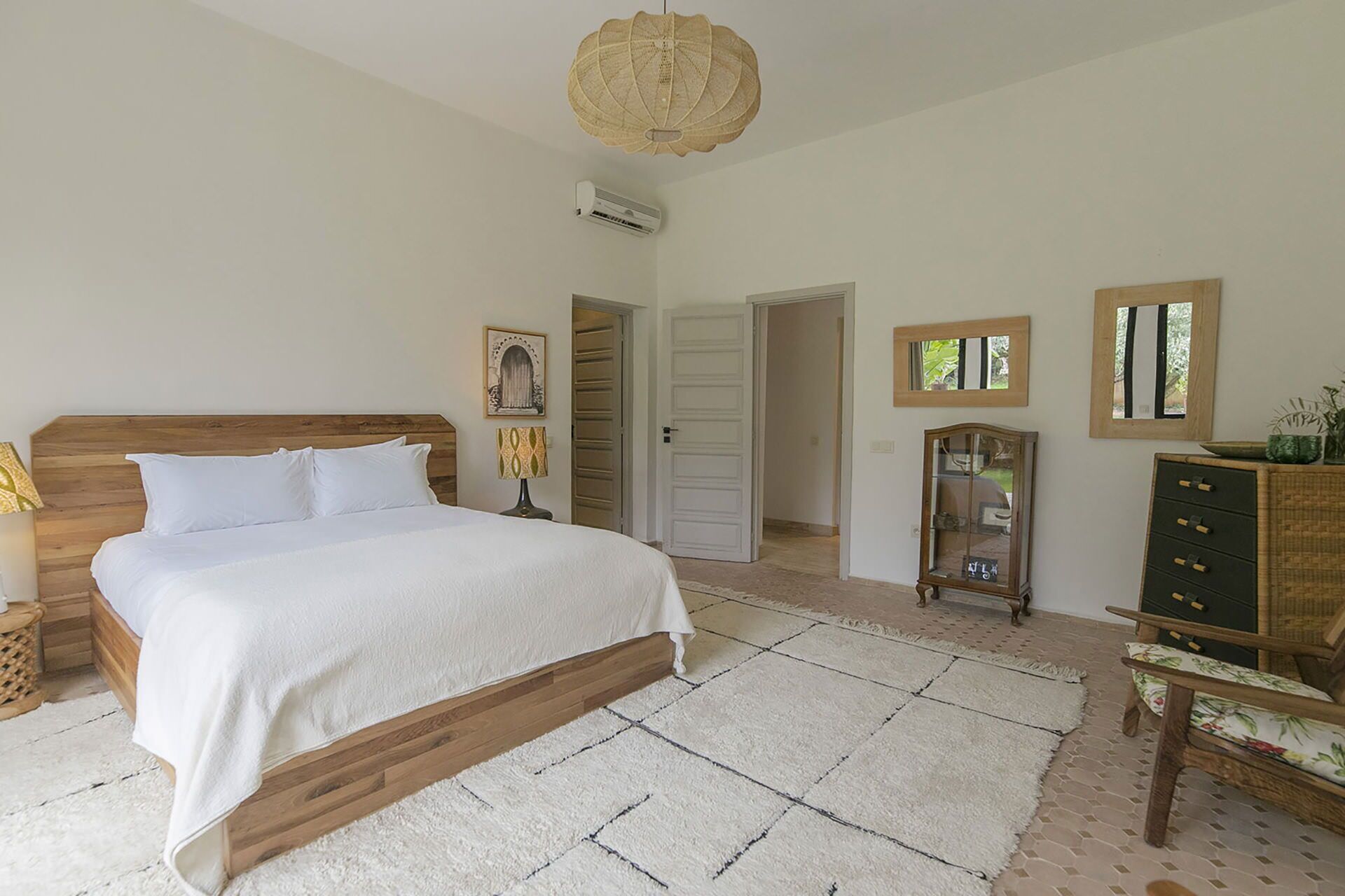 Une chambre à coucher avec un lit en bois, un tapis blanc, une commode et un miroir.