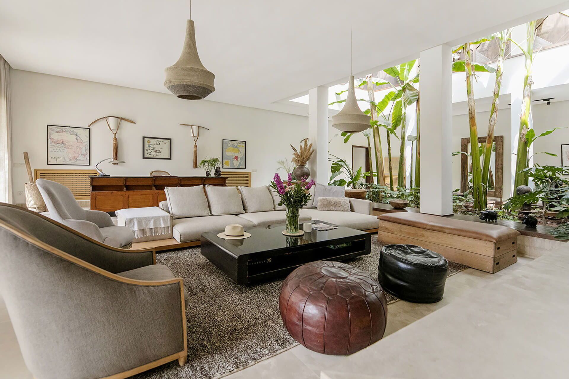 A modern living room with a sofa, coffee table, ottoman, and a large window with plants.