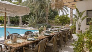 Area pranzo all'aperto con piscina, mobili in vimini e piante tropicali.