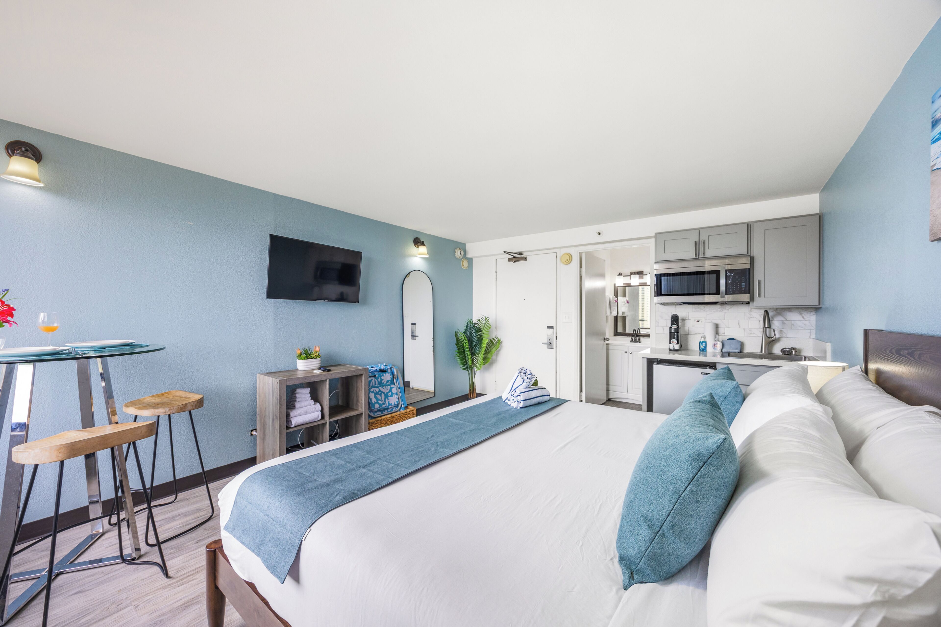 Una habitación de hotel moderna con cama, escritorio, silla, kitchenette pequeña y televisión.