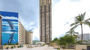 Un hôtel de grande hauteur orné d’une immense fresque représentant des baleines, doté d’un espace piscine et bordé de palmiers.