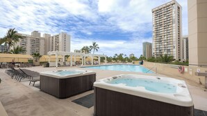 Un espace piscine aménagé sur le toit, avec des jacuzzis, des chaises longues et une vue sur les gratte-ciel.