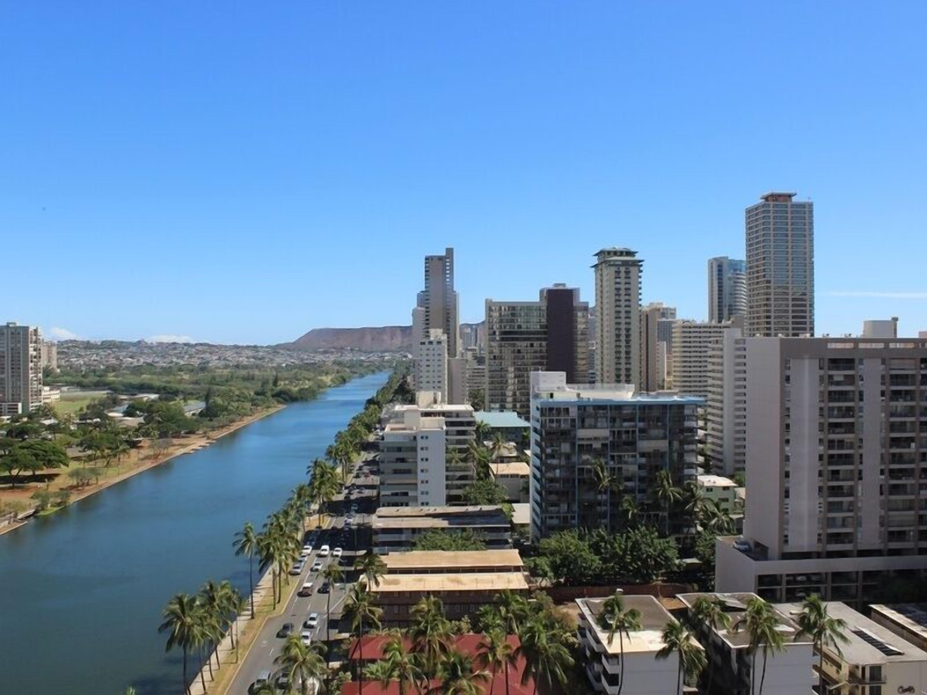A cityscape with a river, high-rise buildings, and palm trees.