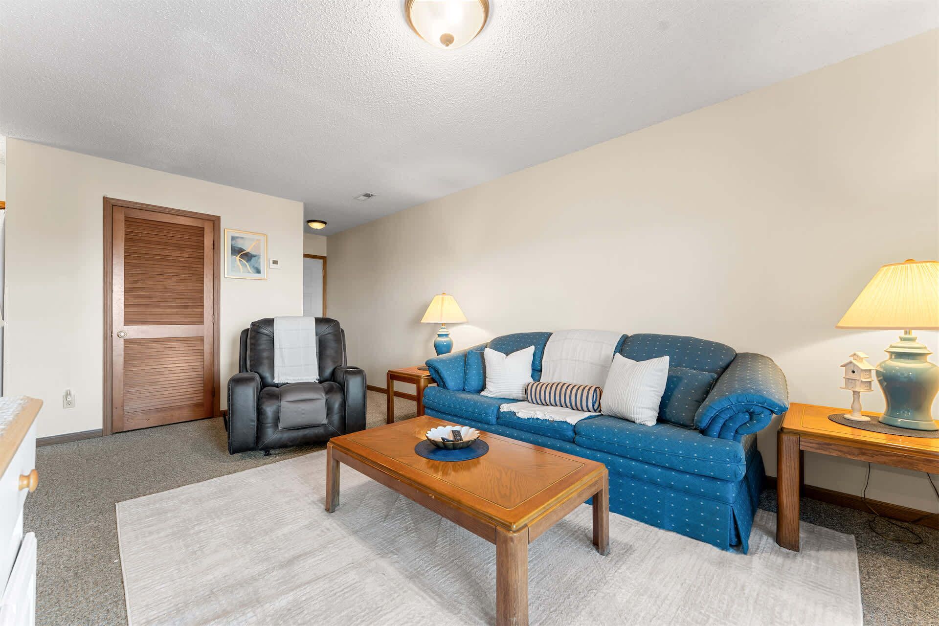 A living room with a sofa, a massage chair, a wooden coffee table, and two lamps.