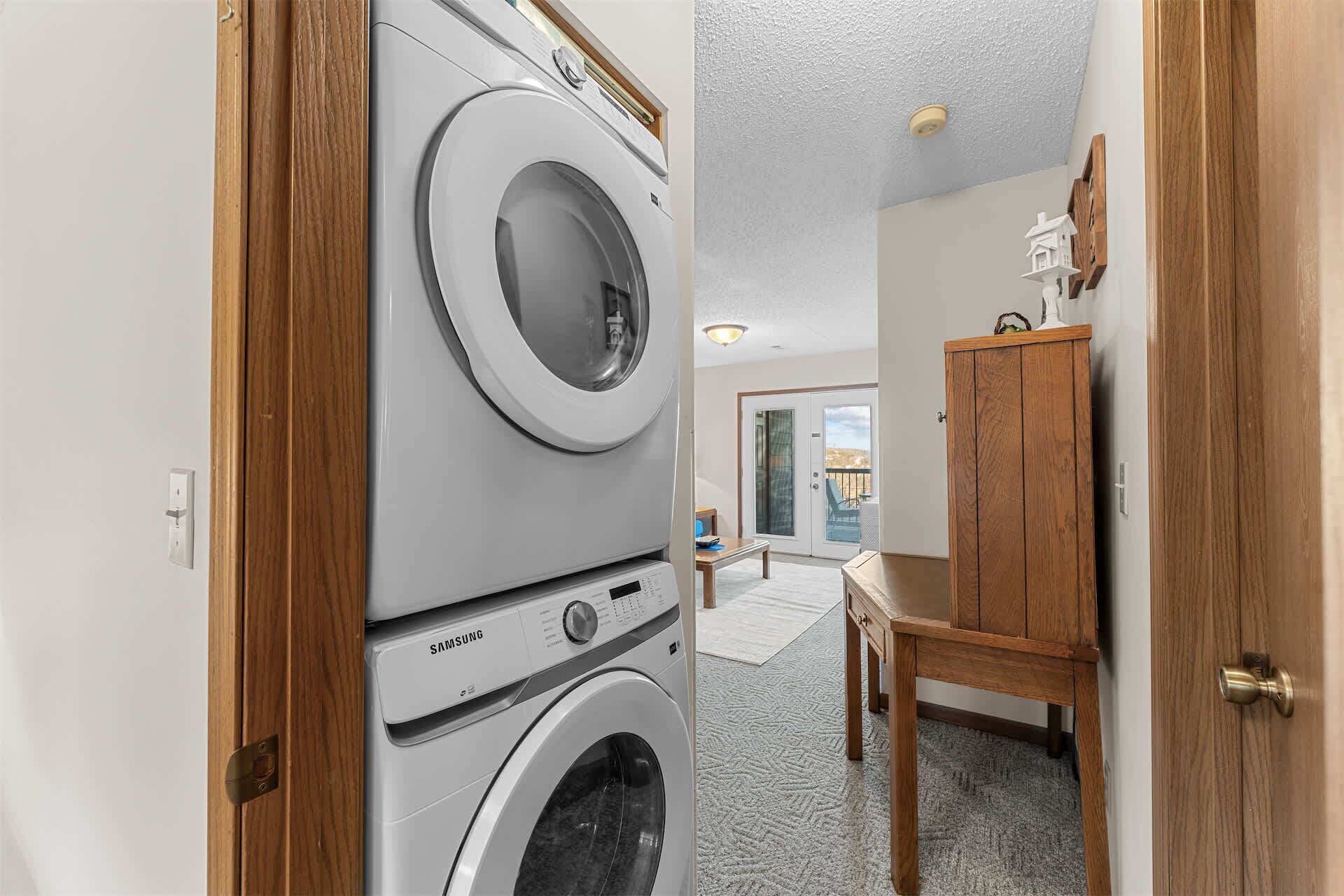 A laundry room with stacked washers and dryers, a wooden cabinet, and a view of the outside.
