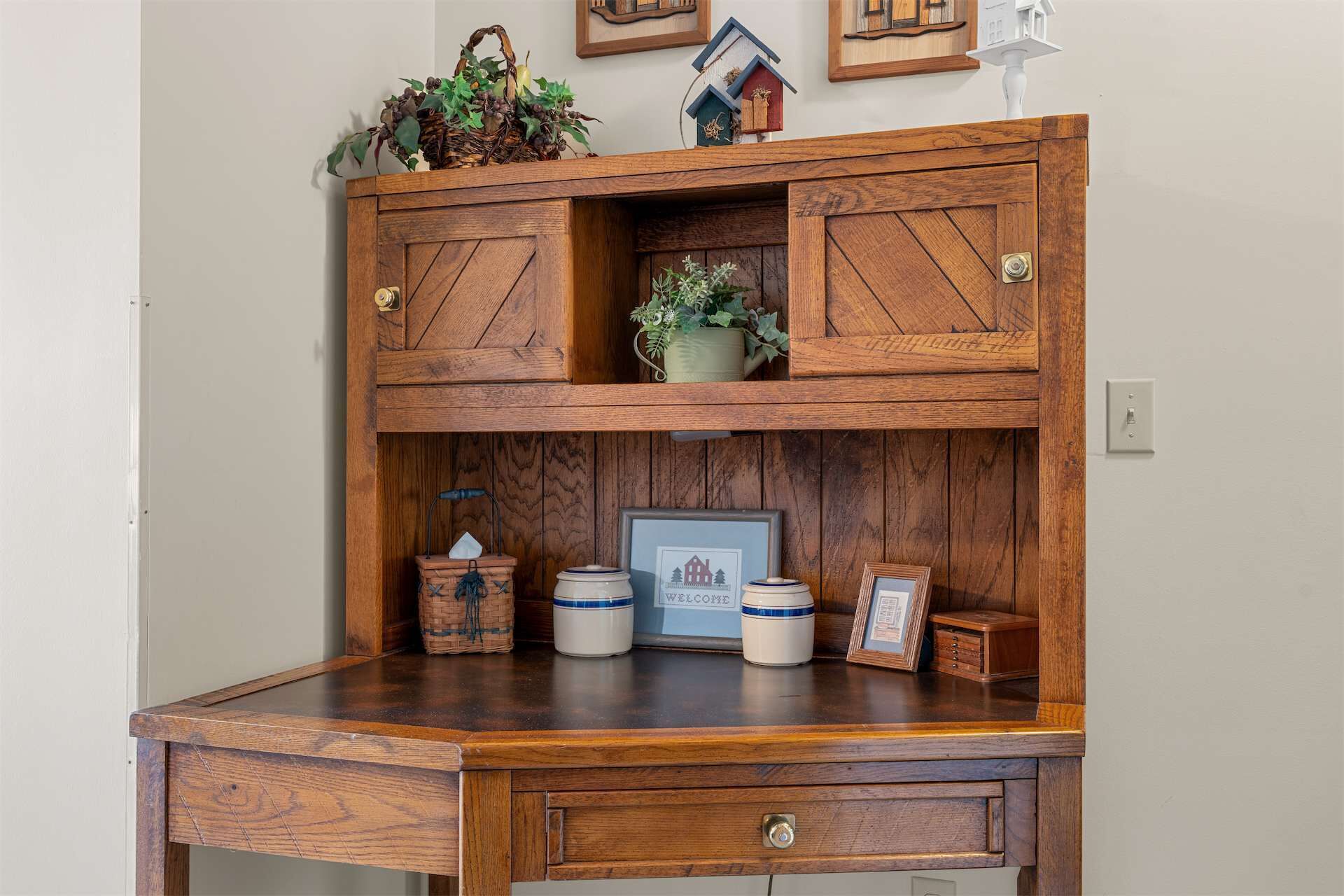 A wooden desk with a built-in cabinet, a framed welcome sign, and decorative jars.