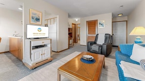 Quarto de hotel com televisão, sofá, poltrona, mesa de centro e abajur.