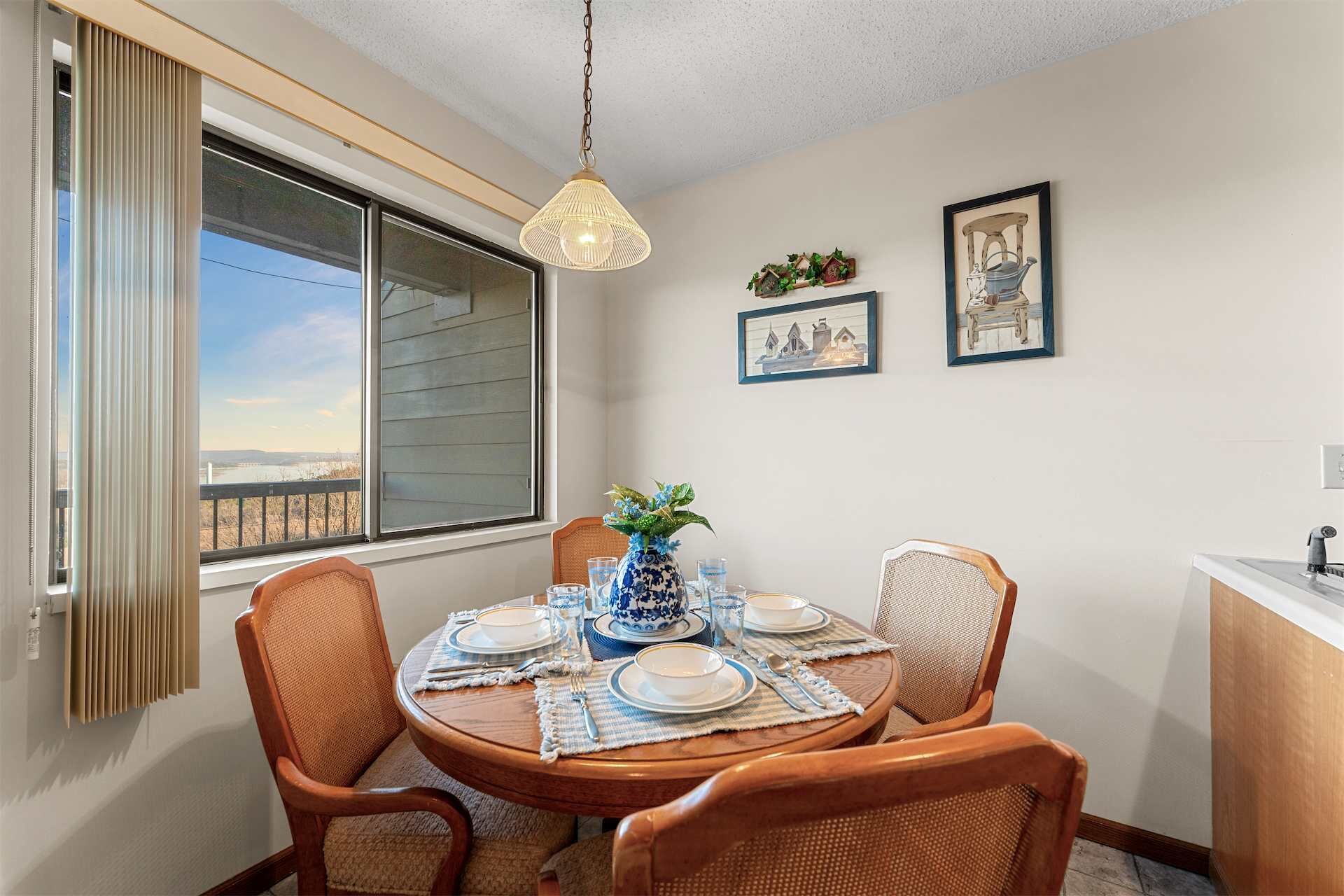 A dining area with a round table, four chairs, a vase with flowers, and a view of a body of water through a large window.