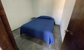 A small, dimly lit room with a single bed, a small table, and a door. - Casa Rosas - 12BR Large Group Rental with Private Pool (San Felipe)