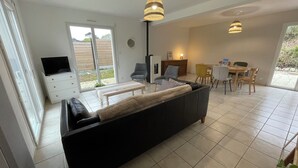 Una sala de estar moderna con un sofá negro, una zona de comedor con sillas amarillas y un televisor sobre un mueble blanco.