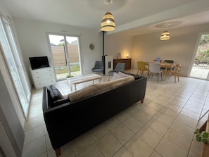 Een moderne woonkamer met een zwarte bank, een eethoek met gele stoelen en een televisie op een witte kast.