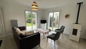 Una sala de estar con un sofá, sillones, un televisor, chimenea y un ventanal corredizo que da a un jardín.