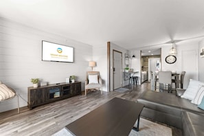 A modern living room with a sofa, coffee table, and TV. There's a dining area with chairs and a kitchen in the background. - Branson Heights Retreat (Branson)