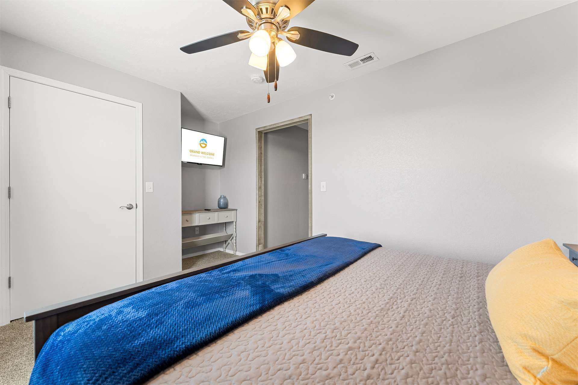 A bedroom with a bed, a ceiling fan, a TV on the wall, and a door leading to another room.