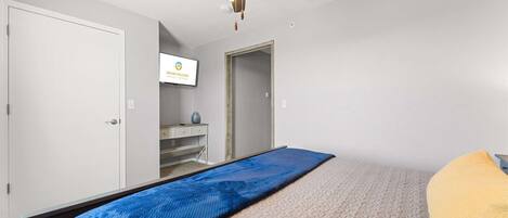 A bedroom with a bed, a ceiling fan, a TV on the wall, and a door leading to another room.