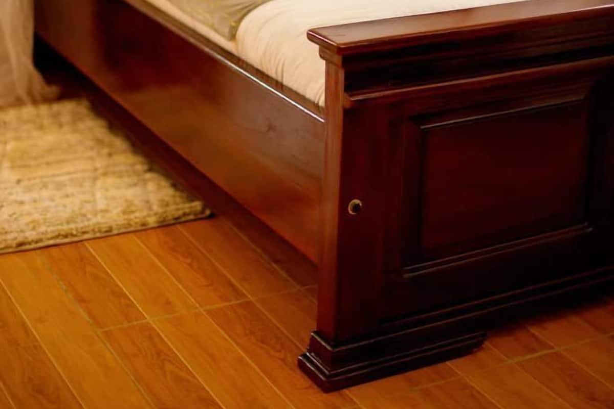 Ein hölzernes Bett mit Kopfteil, weißer Bettwäsche und einer beigen Tagesdecke.