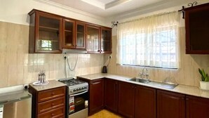 Una cocina con armarios de madera, estufa, fregadero y ventana con cortinas.