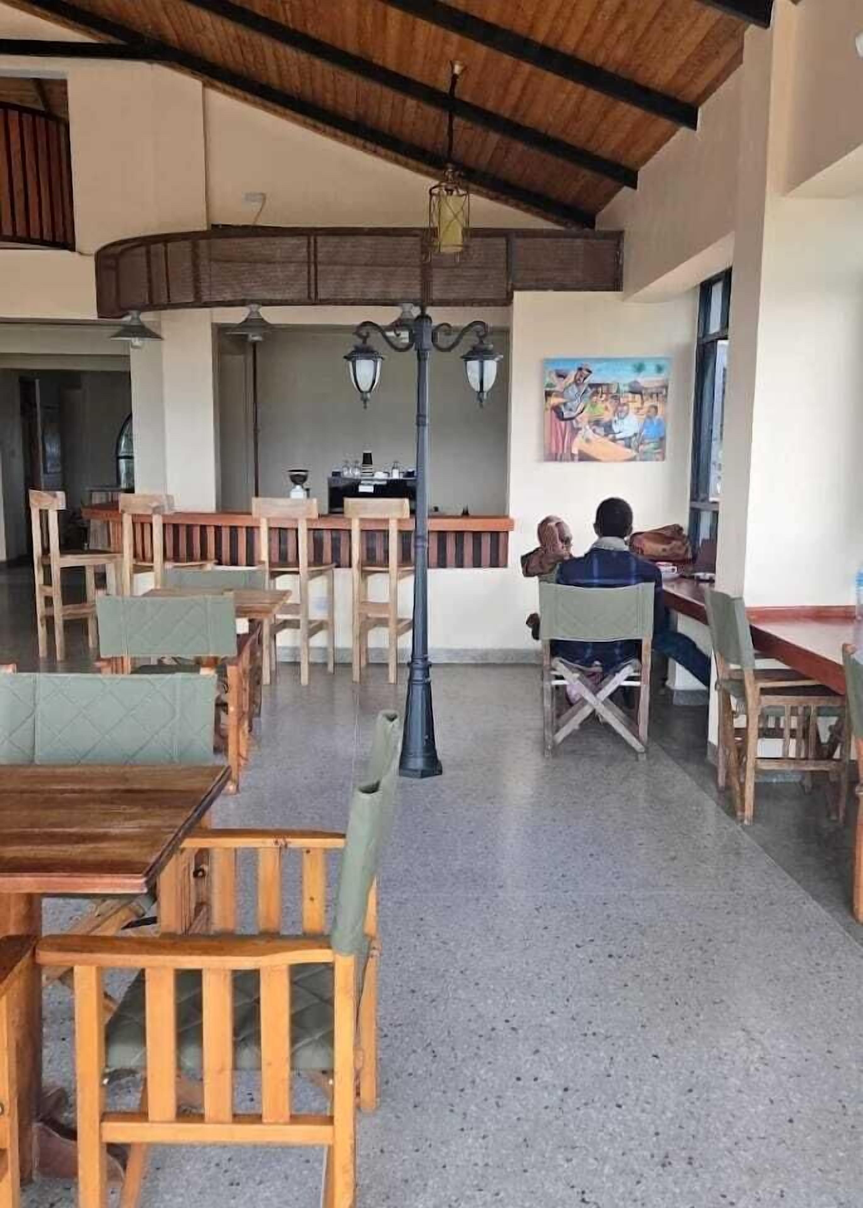 Un restaurante con mesas y sillas de madera, una zona de bar y un cuadro en la pared.