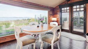 A wooden interior with a round table, two chairs, a vase with flowers, and a view of the outdoors. - Ocean View Guest House - stunning Ocean Views by Victoria Prime!! (Saanichton)