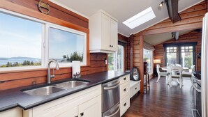 A modern kitchen with a large window, wooden walls, and a view of the outdoors. - Ocean View Guest House - stunning Ocean Views by Victoria Prime!! (Saanichton)