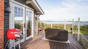 A wooden deck with a grill, wicker chair, and a view of a lake. - Ocean View Guest House - stunning Ocean Views by Victoria Prime!! (Saanichton)