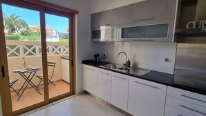 Een moderne keuken met roestvrijstalen apparatuur, een zwart aanrecht en een glazen schuifdeur die leidt naar een buitenruimte met een tafel en stoelen.