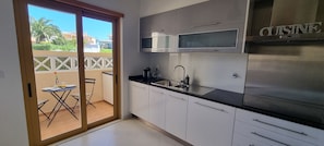 A modern kitchen with stainless steel appliances, a black countertop, and a sliding glass door leading to an outdoor area with a table and chairs. - Vila Rosal standing Ocean view, 300m near to the magnificent Praia São Rafael (Albufeira)
