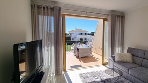 Een woonkamer met een televisie, bank en een balkon met eethoek.
