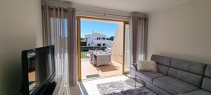 A living room with a TV, sofa, and a balcony with a dining area. - Vila Rosal standing Ocean view, 300m near to the magnificent Praia São Rafael (Albufeira)