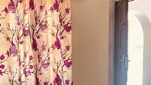 Una habitación con un banco, una puerta que da al exterior y un cortinaje estampado con motivos florales.