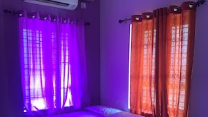 Un dormitorio con cama, cortinas moradas, un aire acondicionado y una ventana con cortinas naranjas.
