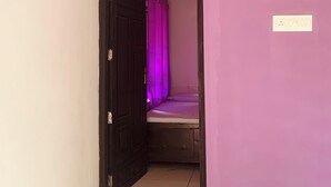 A narrow hallway with a door leading to a room with a bed and purple lighting. - Violin Homestay Cozy Coastal Retreat (Varkala)