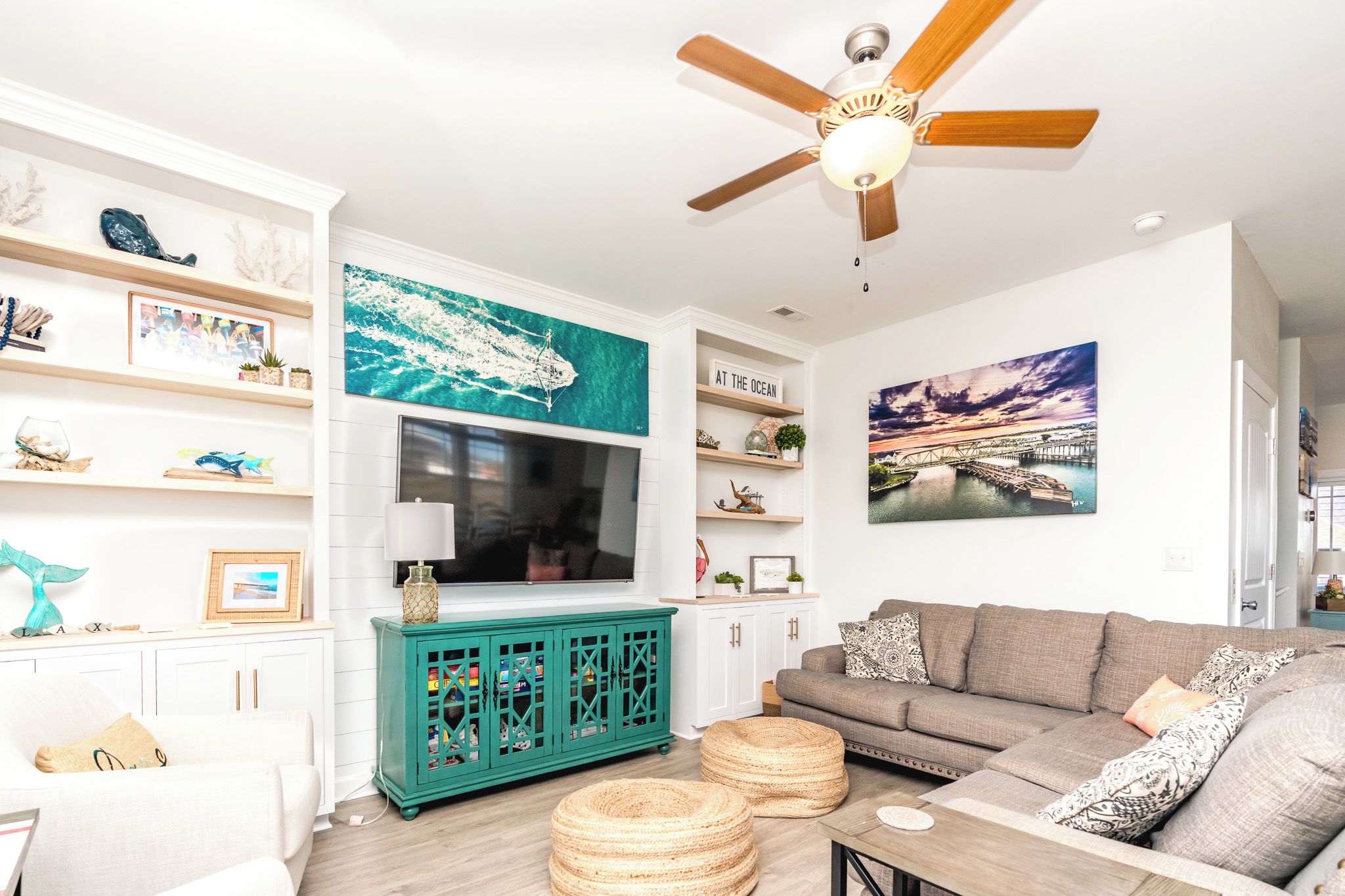 A living room with a television, a teal cabinet, a gray sofa, and a ceiling fan.