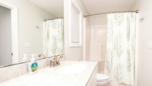 A bathroom with a double sink, a shower, and a window with blinds. - Topsail Fairytale - with sweeping ocean views from three front decks! (Surf City)