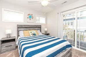 Quarto com cama, duas mesas de cabeceira, ventoinha no teto e vista para o exterior.
