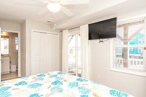 A bedroom with a bed, a TV mounted on the wall, a ceiling fan, and a window with blinds. - Topsail Fairytale - with sweeping ocean views from three front decks! (Surf City)