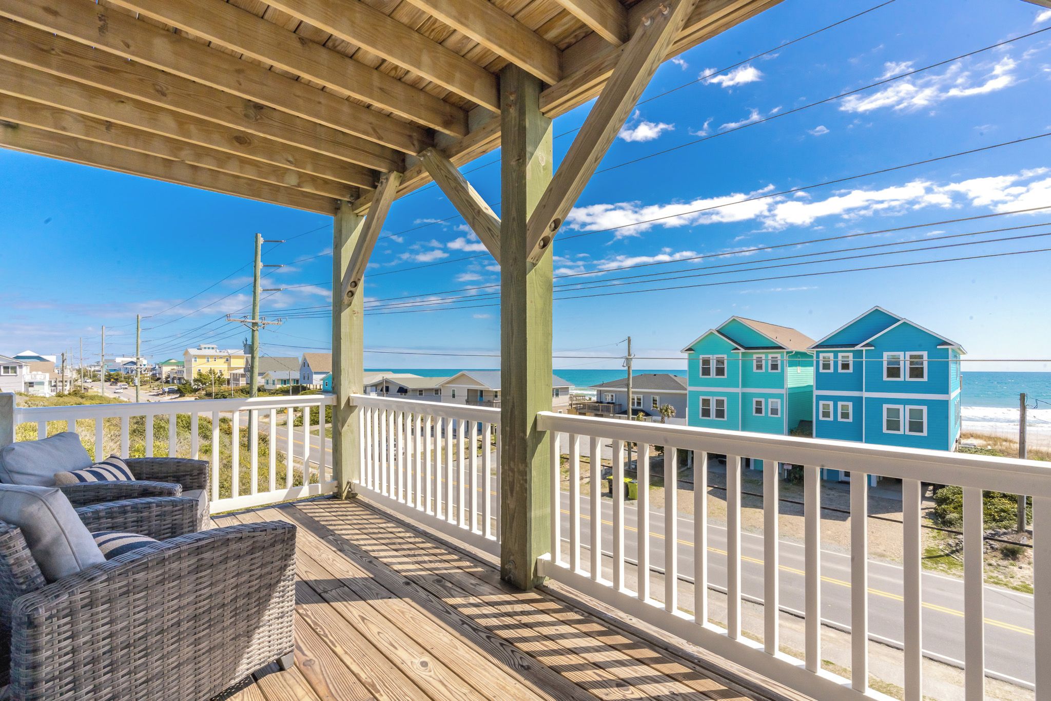 A wooden deck with a white railing, overlooking a beach with two turquoise houses.