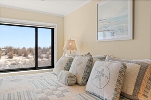 Ein Schlafzimmer mit einem großen Fenster, einem Bett mit gemusterten Bettwaren, einer Lampe und einem gerahmten Bild an der Wand.