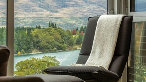 Una silla con una toalla blanca sobre el respaldo, ubicada cerca de una ventana con vista a un lago y colinas boscosas.