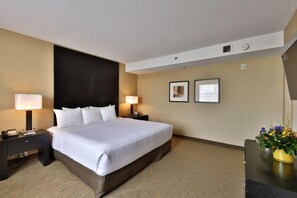 Habitación de hotel con una cama grande, dos mesitas de noche con lámparas, un escritorio con un florero y cuadros en la pared.